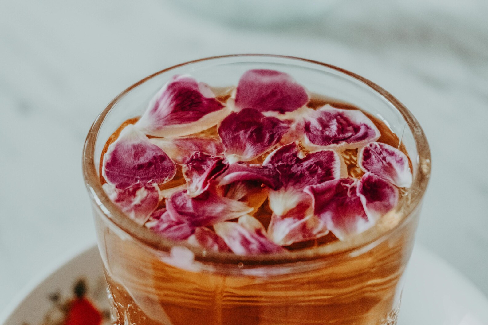 A clear cup of amber tea with floating rose petals